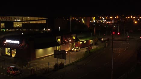 Cars-queue-outside-McDonalds-fast-food-drive-through-at-night-in-Northern-UK-town-aerial-descending-view
