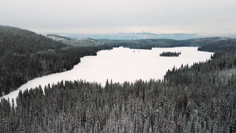 Winter-Dreamscape:-Snowy-Spruce-Trees-Near-Long-Island-Lake-and-Little-Fort-Highway-24-on-a-Cloudy-Day,-with-Mountains-in-the-Distance---Aerial-Pan-Left-View