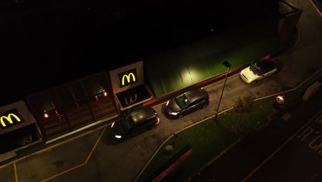 Cars-parked-waiting-at-McDonalds-fast-food-drive-through-at-night-aerial-view-rising