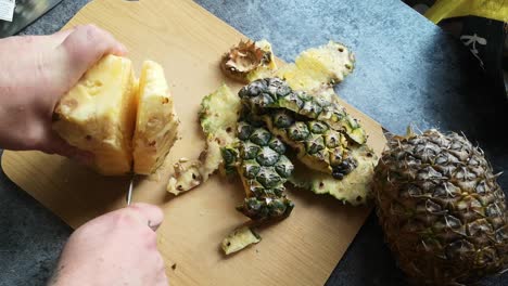 Male-hands-cutting-juicy-ripe-pineapple-with-sharp-knife-on-wooden-kitchen-chopping-board