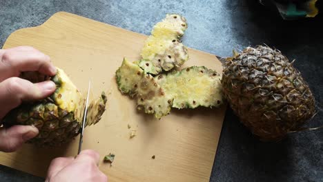 Tattooed-male-hands-cutting-juicy-ripe-pineapple-with-sharp-knife-on-wooden-kitchen-chopping-board