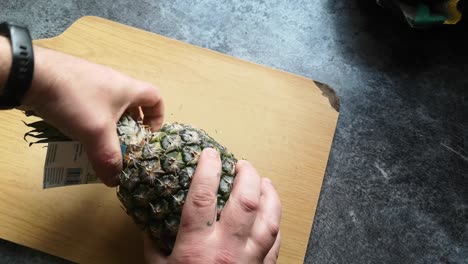 Männliche-Hände,-Die-Reife-Ananasoberseite-Auf-Hölzernem-Küchenschneidebrett-Entfernen