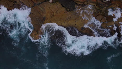Above-drone-shot-of-rocks-being-lapped-with-waves