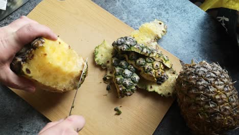 Male-hands-cutting-juicy-ripe-organic-pineapple-with-sharp-knife-on-wooden-kitchen-chopping-board