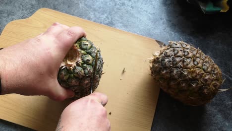 Male-hands-cutting-juicy-ripe-pineapple-skin-with-sharp-knife-on-wooden-kitchen-chopping-board