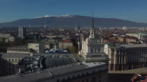 Drone-shot-of-Sofia-in-Bulgaria---drone-is-flying-around-the-Largo-building,-facing-the-mountains