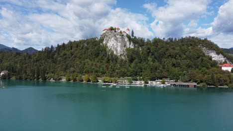 Toma-De-Un-Dron-Del-Lago-Bled-En-Eslovenia---Un-Dron-Está-Cruzando-El-Lago-Hacia-Un-Castillo-En-La-Colina