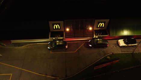Birdseye-as-cars-queue-at-McDonalds-fast-food-drive-through-at-night-in-Northern-UK-town-aerial-orbiting-view