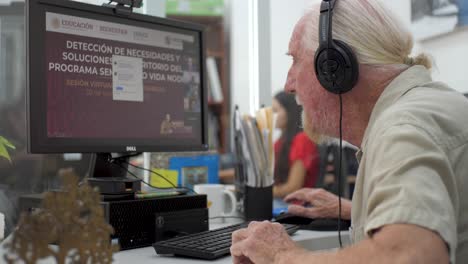 Gray-Haired-Elderly-Man-with-Beard-Wears-Headset-and-Uses-Computer-for-Education-Videoconference-in-Mexico