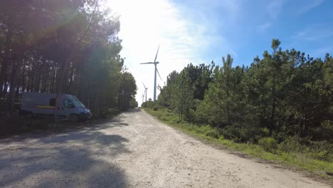 Wohnmobil-Versteckt-Unter-Kiefern-Mit-Windkraftanlage,-Die-Sich-In-Der-Ferne-Dreht,-Nazare,-Portugal