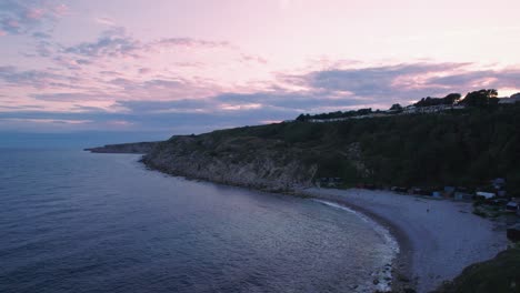 Drone-shot-flying-up-over-a-beach-on-the-Isle-of-Portland-at-sunset,-Dorset,-UK