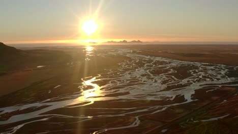 Aerial-shot-over-Icelands-braided-rivers-with-the-sunset-and-Vestmannaeyjabær-island-in-the-background