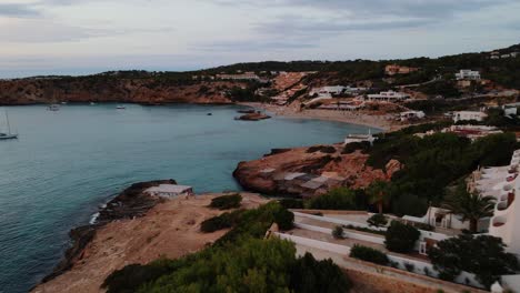 Aerial-Dolly-Over-Coastline-At-Cala-Tarida-With-Tilt-Down-View-Of-Small-Bay-In-Late-Afternoon
