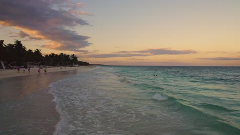 Lufttiefflug-über-Karibischen-Meereswellen-Am-Akiin-Strand-In-Tulum,-Mexiko-Während-Des-Sonnenuntergangs-Mit-Menschen,-Die-Ihren-Strandurlaub-Genießen