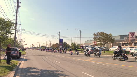 Police-Motorcycle-unit-parade-along-road-at-funeral-honors-for-police-officer,-tracking-in-shot