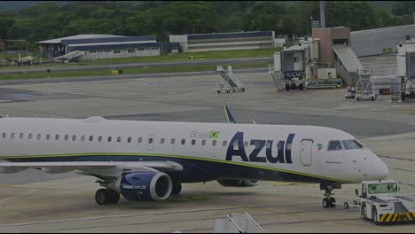 Azul-airlines-aircraft-jet-being-positioned-for-takeoff-by-a-towing-tractor-at-the-airport-gate