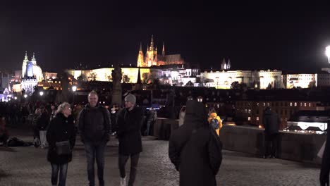People-walking-on-Charles-bridge-on-winter-night,-Prague-castle-beyond