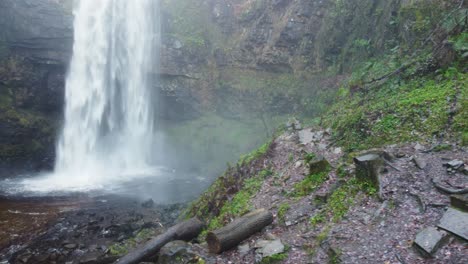 Seitliche-Luftdrohne-Eines-Dramatischen-Wasserfalls-Mit-Warnzeichen-Und-Gehackten-Baumstämmen-4k