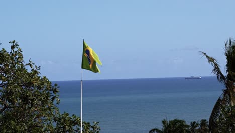 Brazil-flag-close-up-waving-in-the-wind-in-120fps-slow-motion-with-the-vast-ocean-in-the-background-in-the-historic-city-of-Olinda-in-Pernambuco,-Brazil-on-a-warm-sunny-clear-summer-day