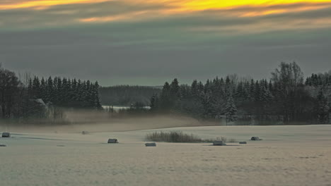 Timelapse-Of-Winter-Snow-Farmland-Landscape-With-Rolling-Mist-Moving-Over-Against-Orange-Sunset-Sky