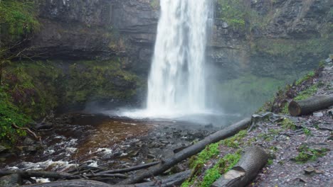 Wasserfall-Seitlich-Luftdrohnenaufnahme-Von-Stürzendem-Wasser-Mit-Baumstämmen-Und-Klippen-In-Wales-UK-4k