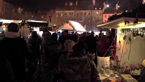 People-strolling-between-Christmas-market-stalls-at-night,-Prague-city