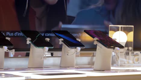 Slow-rotating-shot-of-new-smartphone-technology-on-display-with-an-animated-billboard-behind