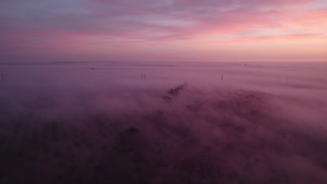 Colorful-sunrise-with-mist-covering-countryside-landscape,-aerial