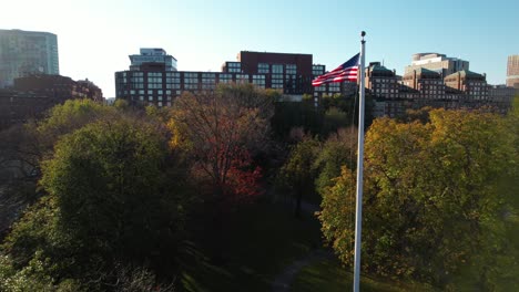 Aerial-view-rising-up-American-national-flag-waving-in-Boston-public-garden-on-windy-morning