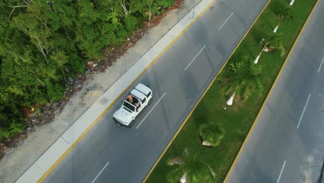 Drone-shot-view-of-white-car-driving-on-road-in-Tulum,-Mexico