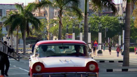 Colorfully-restored-vintage-American-classic-automobiles-driving-down-a-street-in-Havana,-Cuba