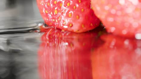 Strawberries-reflected-on-mirror,-Water-drops-fall-and-create-a-ripple,-Slow-motion