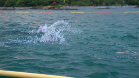 Slow-motion-close-up-of-two-swimmers-competing-in-a-triathlon-in-the-sea-wearing-pink-caps-and-goggles