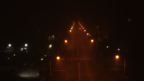 Foggy-night-in-the-city,-drone-flying-over-empty-road-with-street-lights