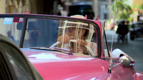 Man-wearing-a-Panama-hat-and-driving-a-pink-vintage-car-in-Havana,-Cuba