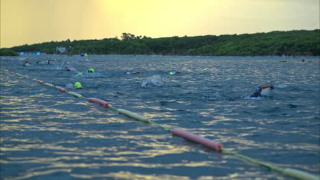 Slow-motion-wide-shot-of-swimmers-athletes-competing-in-a-triathlon-in-the-sea-early-in-the-morning