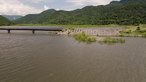 Low-bridge-over-Tkibuli-lake-reservoir-in-Georgia,-lush-valley-beyond