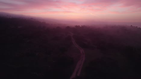 Dramatic-dark-mist-woodland-with-stunning-colorful-sunrise,-aerial