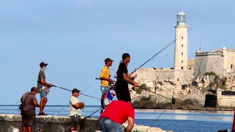 People-fishing-with-the-Faro-Castillo-del-Morro-lighthouse-in-Havana,-Cuba-in-the-background