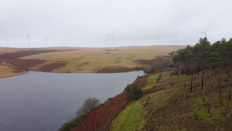 Fast-Panning-Aerial-Drone-shot-over-Reservoir-with-Wind-Turbines-on-Moorland-Hill-Background-4K