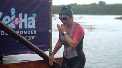 Female-athlete-finishing-the-swimming-stage-at-a-triathlon-watching-her-time-in-her-sports-watch-wearing-cap-and-goggles