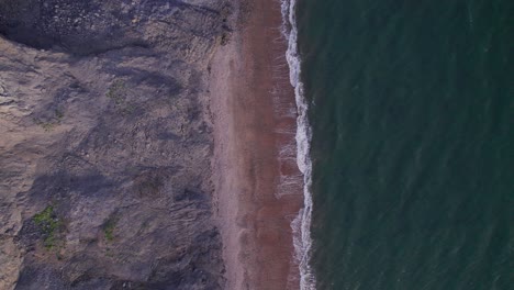 Top-down-drone-shot-moving-down-of-green-sea's-waves-and-cliffs-on-the-Jurassic-Coast,-Dorset,-UK