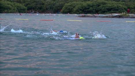 Slow-motion-of-athletes-wearing-caps-and-goggles-swimming-competing-in-a-triathlon-in-the-sea