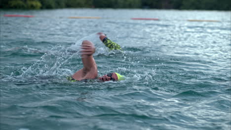 Close-up-shot-in-slow-motion-of-two-swimmers-competing-in-a-triathlon-in-the-sea-wearing-caps-and-goggles
