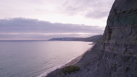 Drone-shot-flying-around-a-cliff-face-to-reveal-the-beach-on-the-Jurassic-Coast,-Dorset,-UK