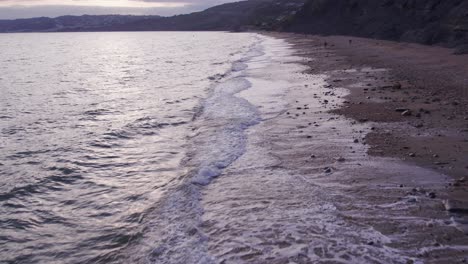 Low-slow-motion-drone-shot-moving-forwards-of-waves-crashing-on-the-beach,-Jurassic-Coast,-Dorset,-UK