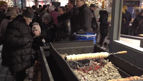 Lady-raking-grill-embers-below-chimney-cake,-Prague-Christmas-market