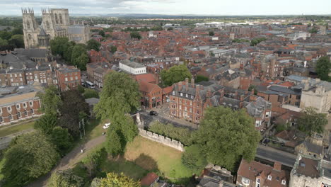 Aerial-Drone-Shot-Flying-Forward-into-York-City-Centre-with-Old-Red-Brick-Buildings-and-York-Minster-Cathedral-in-View-on-Sunny-and-Cloudy-Day-with-Museum-Gardens-Trees-in-Views-North-Yorkshire-UK