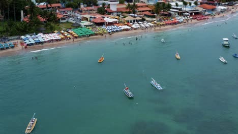 Rising-tilting-down-aerial-drone-shot-of-the-Porto-de-Galinhas-or-Chicken-Port-beach-with-anchored-sailboats-and-hundreds-of-tourists-swimming-in-the-crystal-clear-ocean-water-in-Pernambuco,-Brazil
