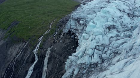 Glacier-melting-creating-streams-of-cold-water-flowing-down-mountain,-aerial
